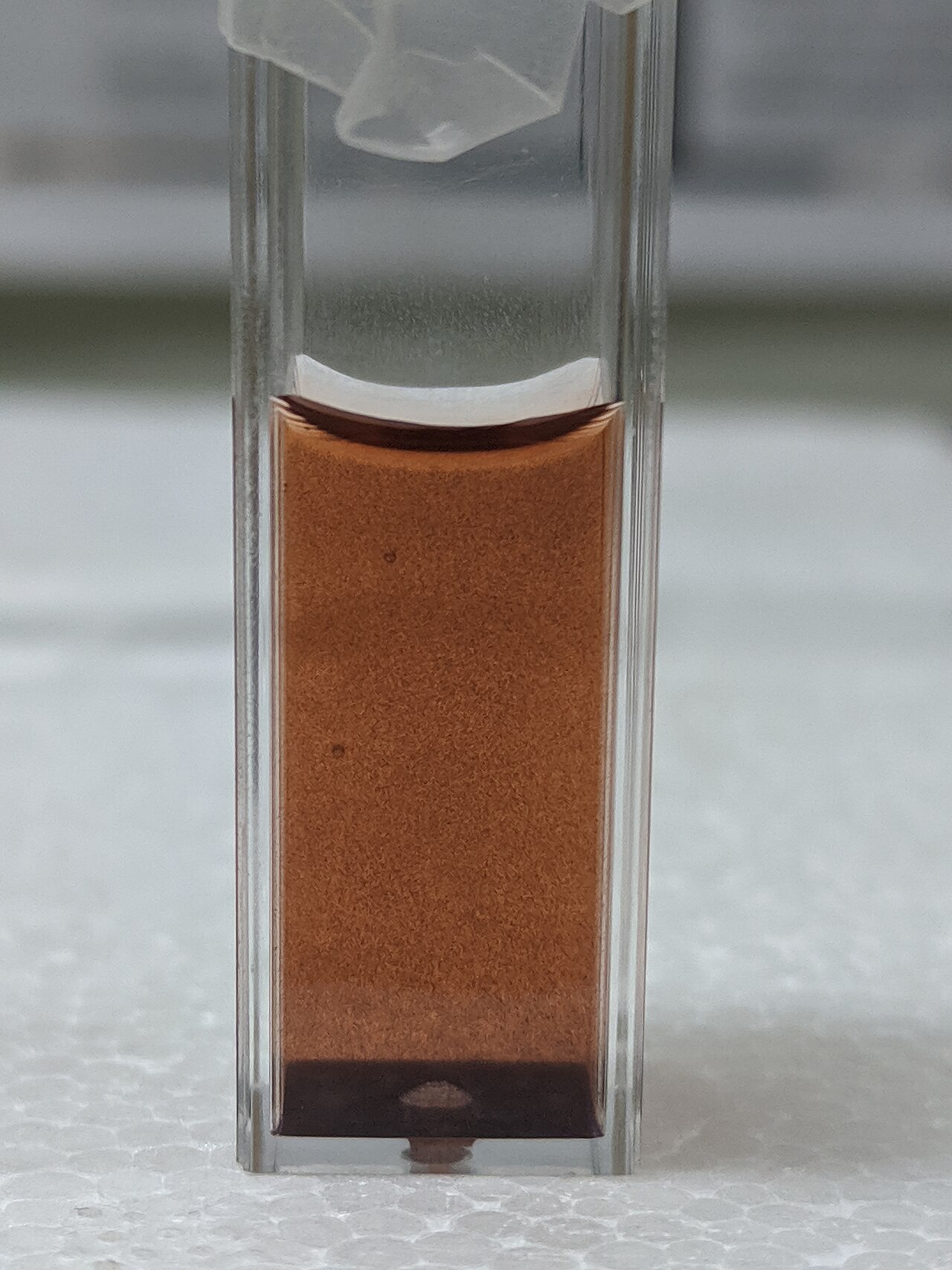 A colloid solution of chemotherapy drug and gold nanoparticles aggregating and creating a residue on the bottom of the quartz cuvette for optical spectrophotometry.